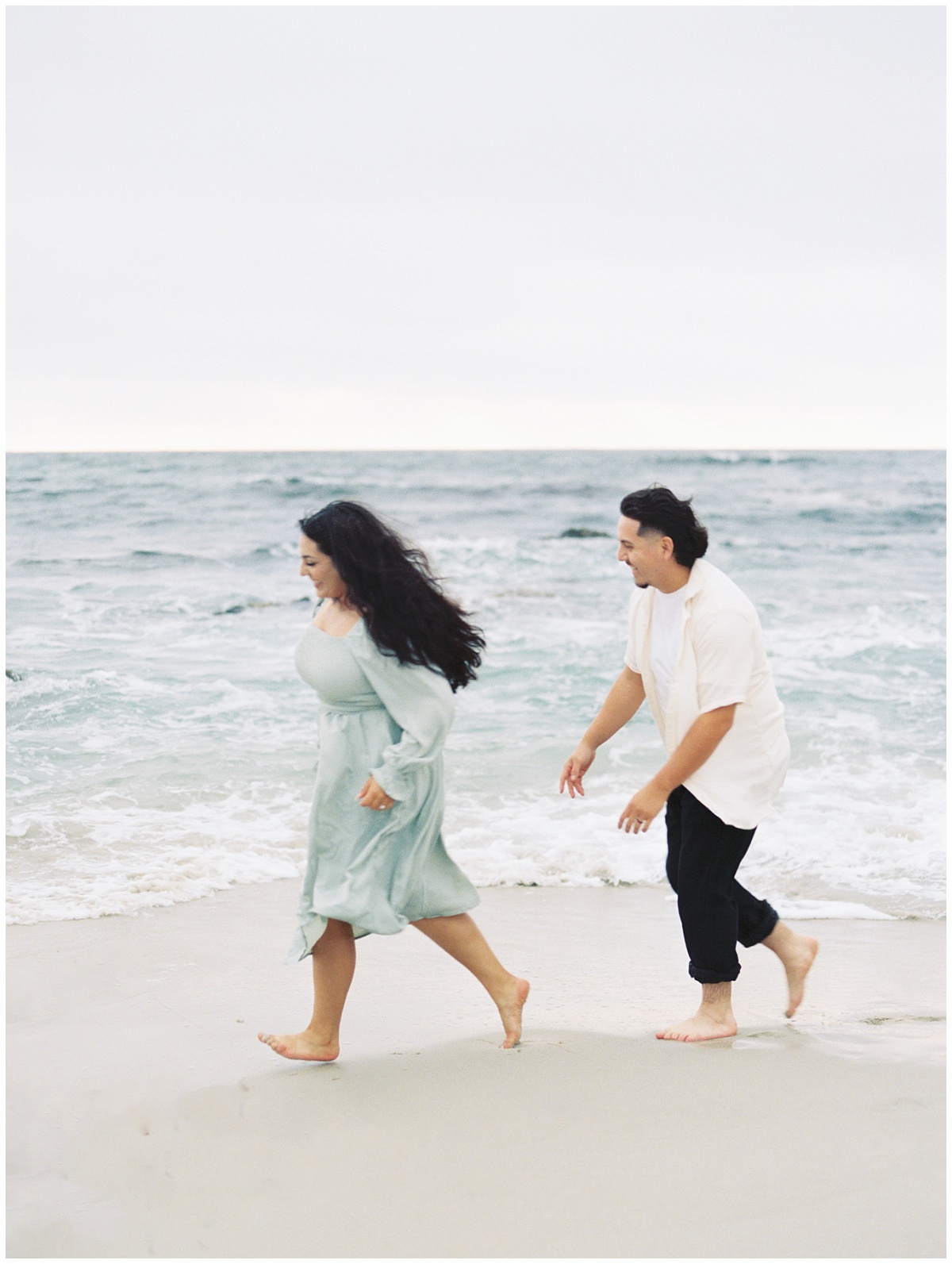 Engagement photo of couple running at the beach playing tag